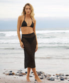 Woman wearing a matching, knit black top and skirt, standing on a beach.