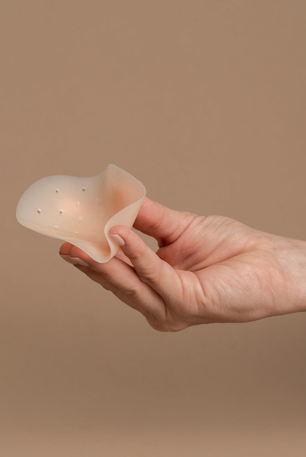 Hand picking up a nipple cover in front of the brown background.