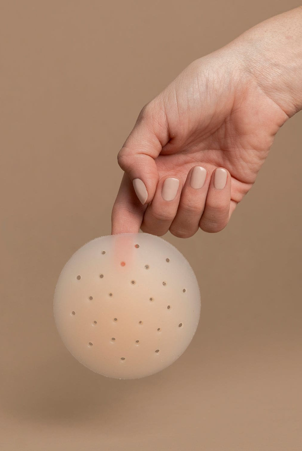 Hand picking up a nipple cover in front of the brown background.