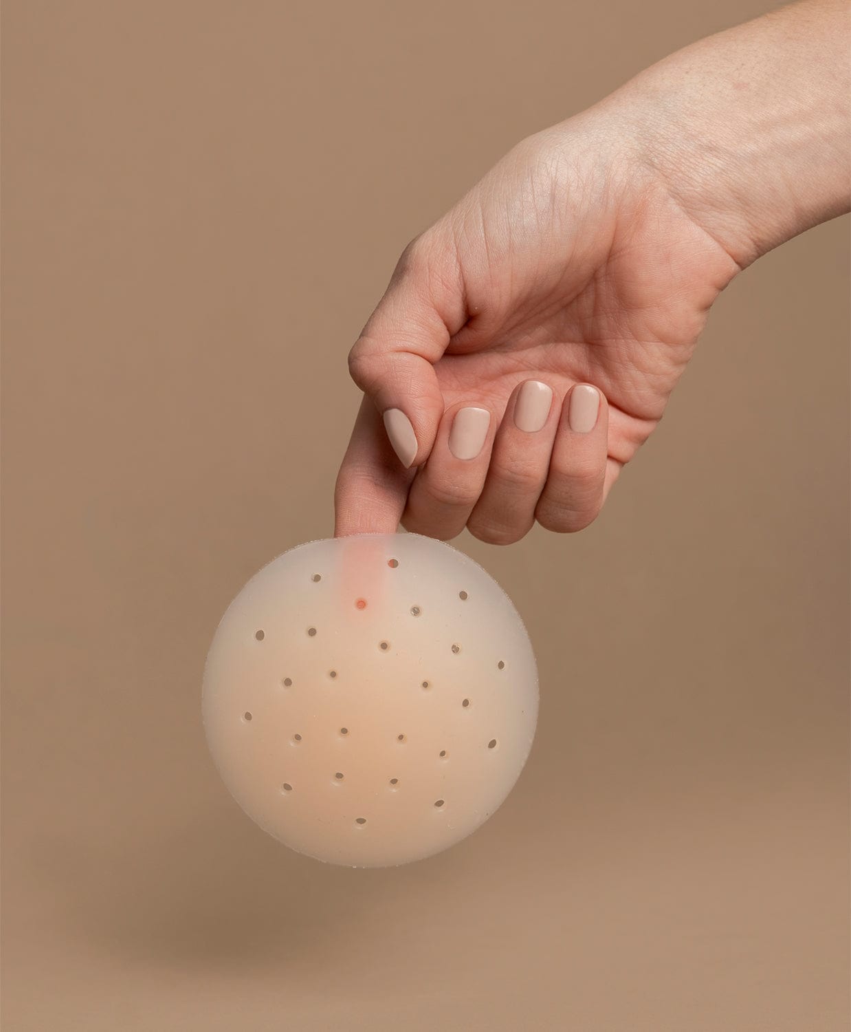 Hand picking up a nipple cover in front of the brown background.