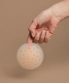 Hand picking up a nipple cover in front of the brown background.