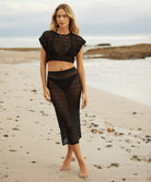 Woman wearing a matching, knit black top and skirt, standing on a beach.