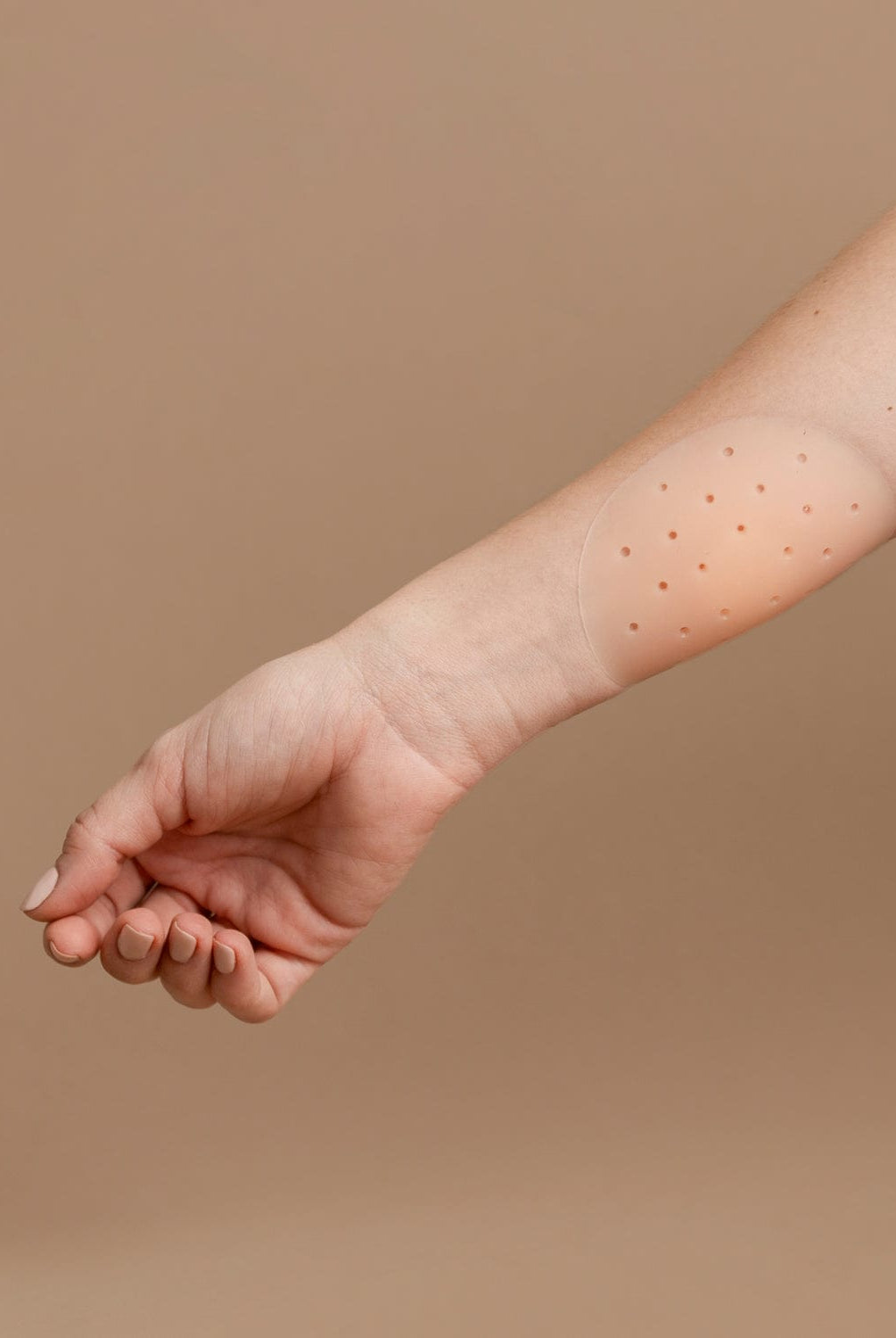 Nipple cover stuck on an arm in front of a brown background.