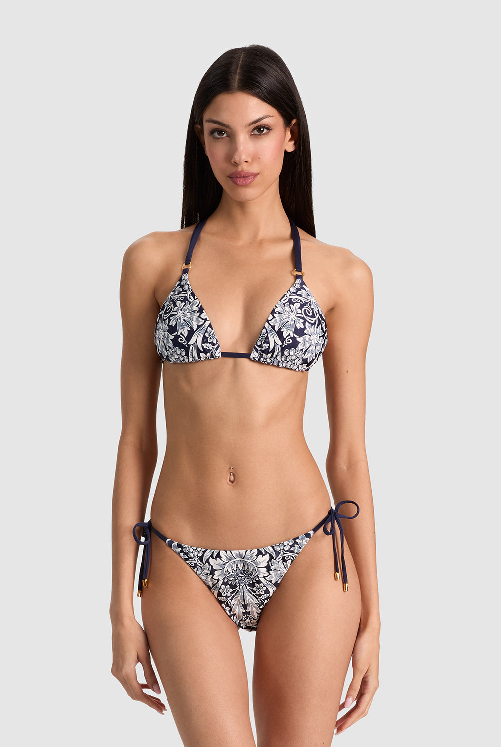 A woman modeling a two-piece string bikini with a navy blue and white floral pattern against a solid light gray background.