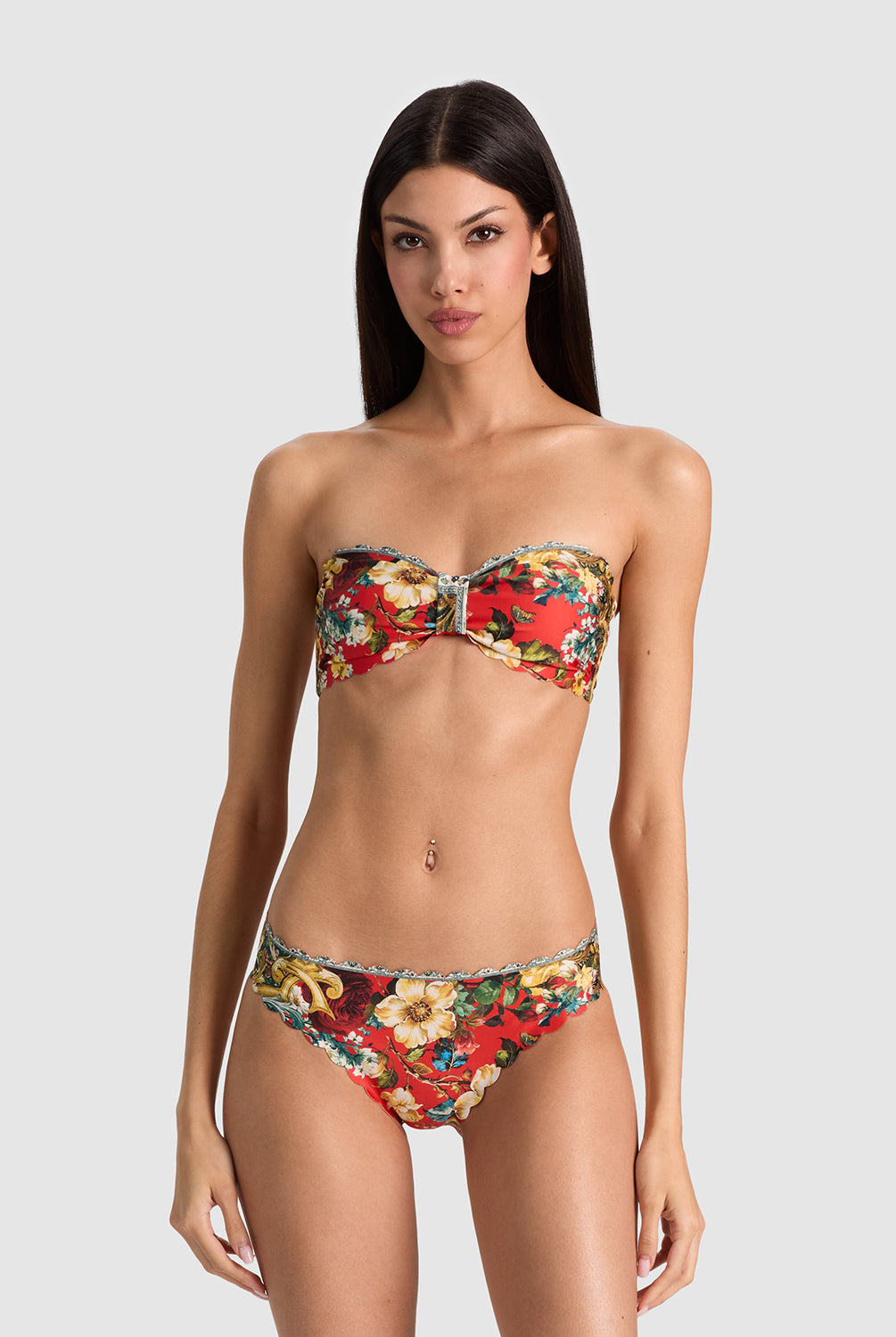 A woman modeling a strapless bikini set with a vibrant red, yellow, and green floral print against a solid light gray background.