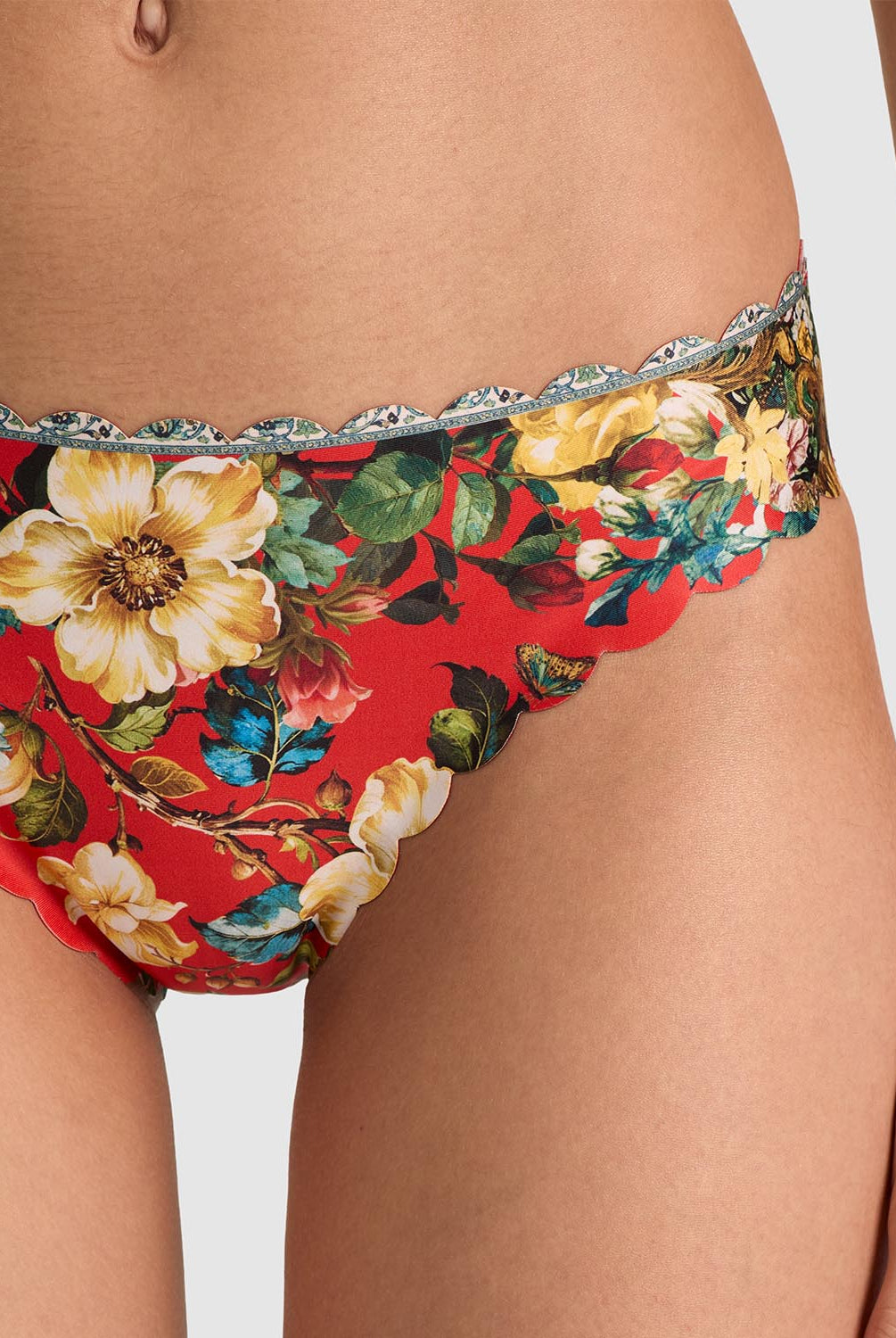 Close-up of a model wearing red floral bikini bottoms with a silver scalloped lace trim, featuring large yellow and white flowers with green leaves.