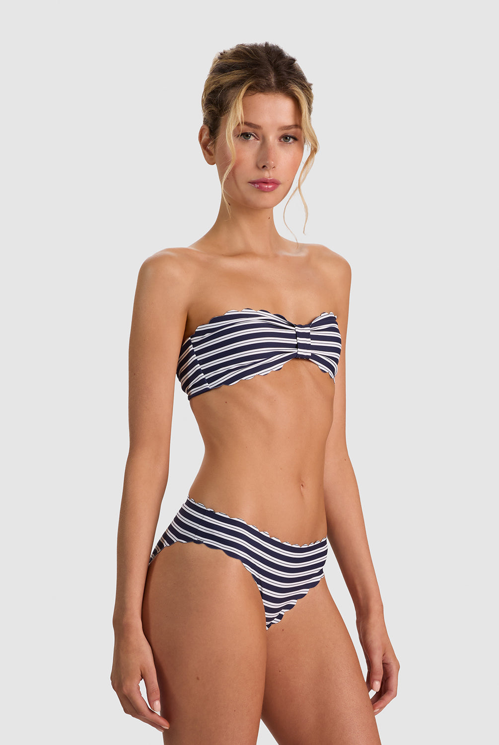 A woman modeling a two-piece bikini with navy and white horizontal stripes against a light gray studio background.