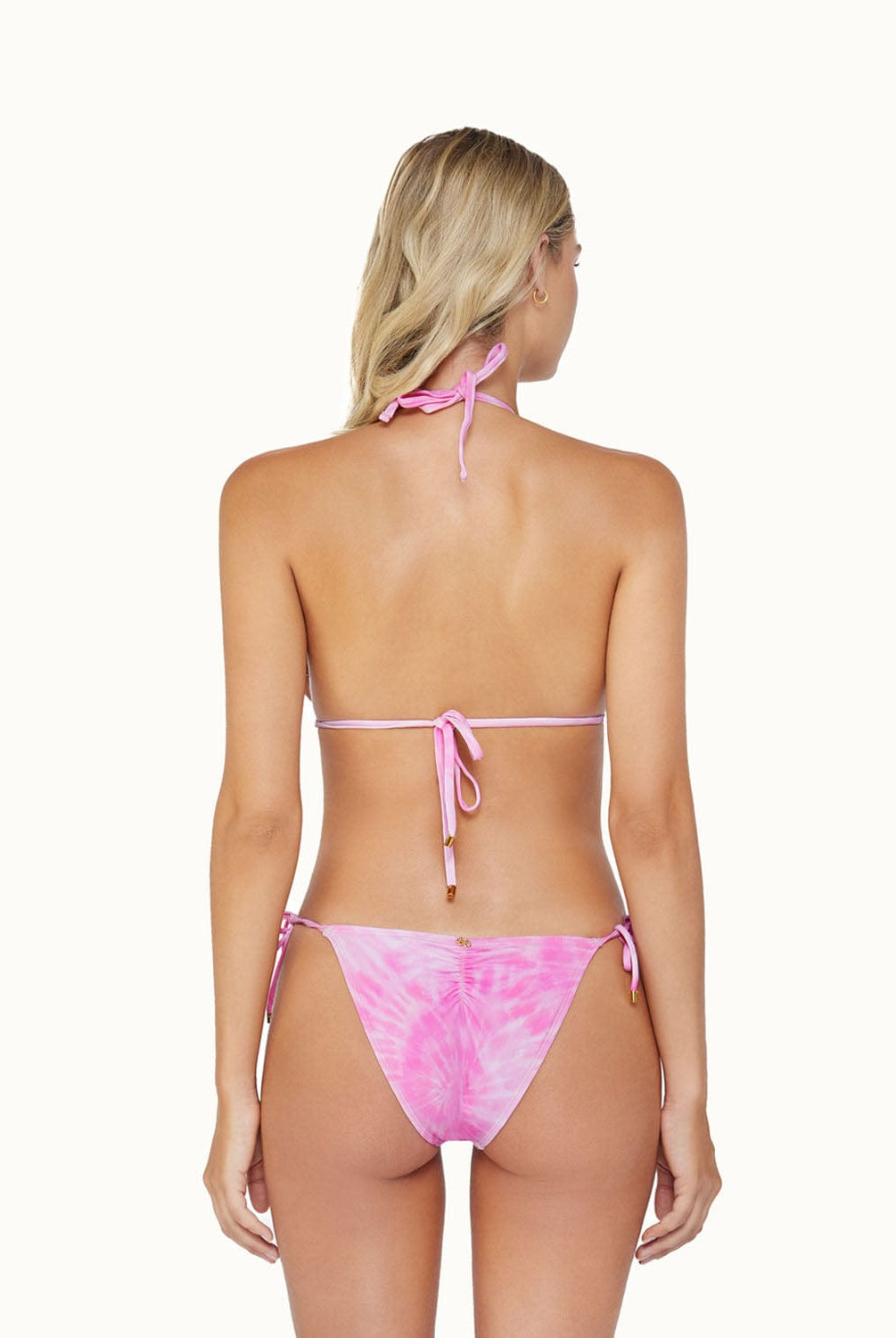 A blonde woman wearing a pink bikini facing towards a white wall.