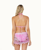 A blonde woman wearing pink lace shorts facing towards a white wall.