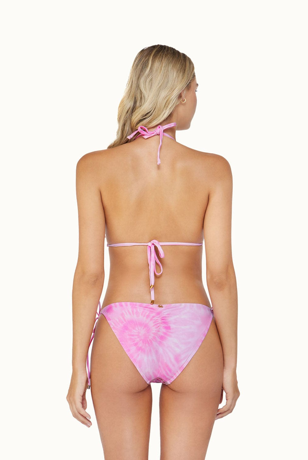 A blonde woman wearing a pink bikini facing towards a white wall.