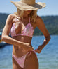A blonde woman wearing a pink lace bikini standing near the water. 