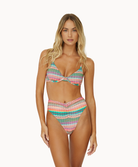 A blonde woman wearing a striped bikini standing against a white wall.
