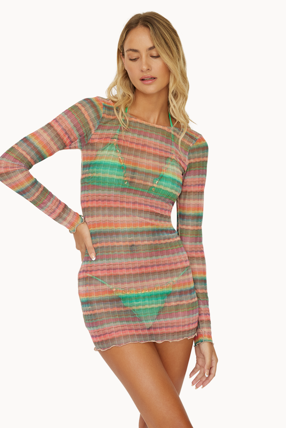 A blonde woman wearing a striped long sleeve dress standing against a white wall.