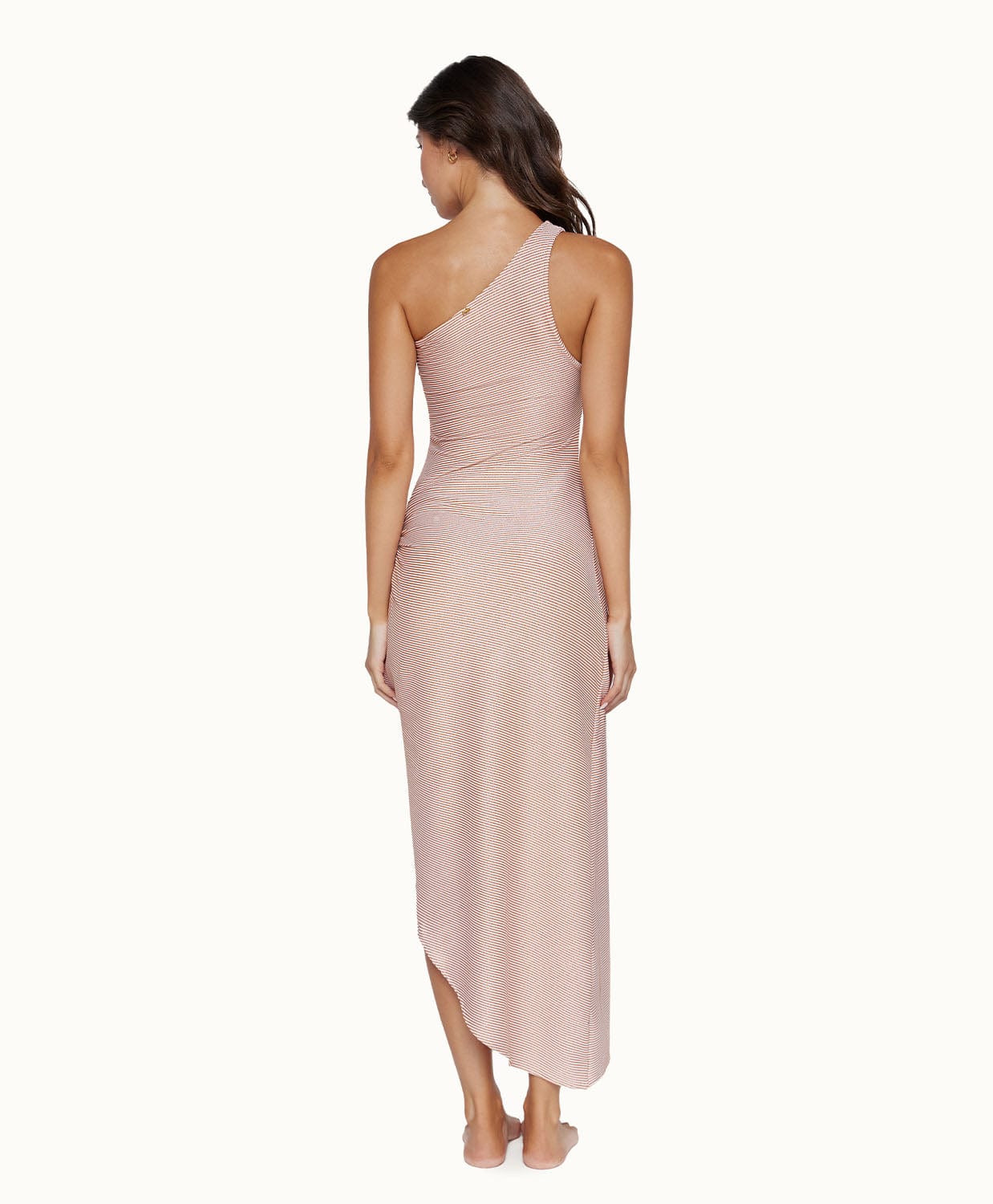 Brunette woman wearing a mid-length dress facing towards a white wall.