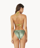 Brunette woman wearing metallic bikini facing towards a white wall.