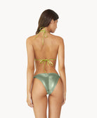 Brunette woman wearing metallic bikini facing towards a white wall.