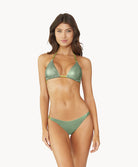 Brunette woman wearing metallic bikini stands in front of white wall.