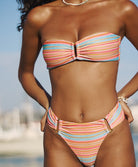 A woman wearing a striped bandeau bikini standing near boats and water.