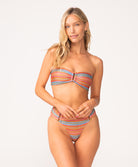 A woman wearing a striped bandeau bikini standing against a white wall.