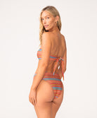 A woman wearing a striped bandeau bikini standing against a white wall.