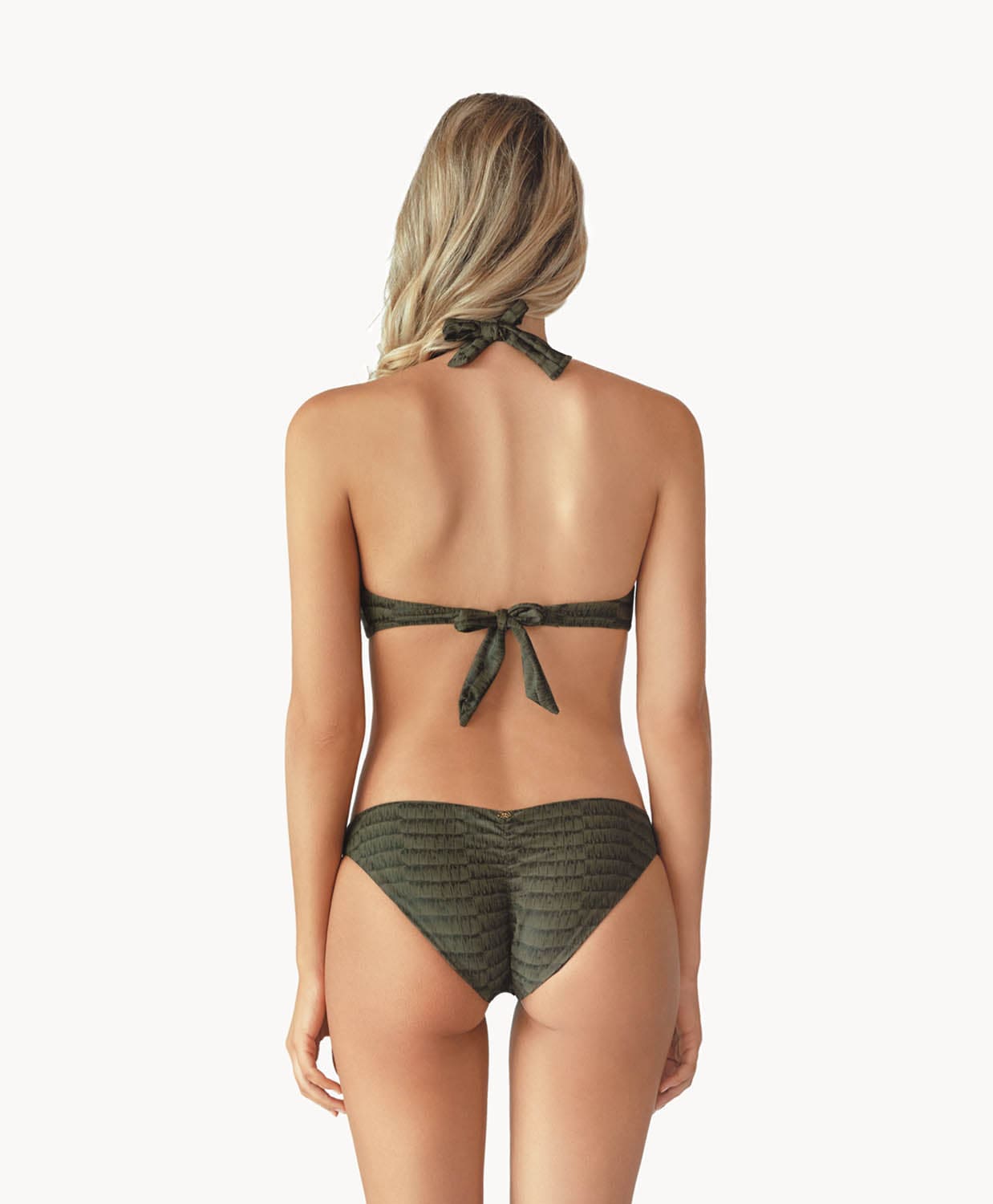 Blonde woman wearing a gray print halter bikini with ring detail facing backwards towards a white wall.