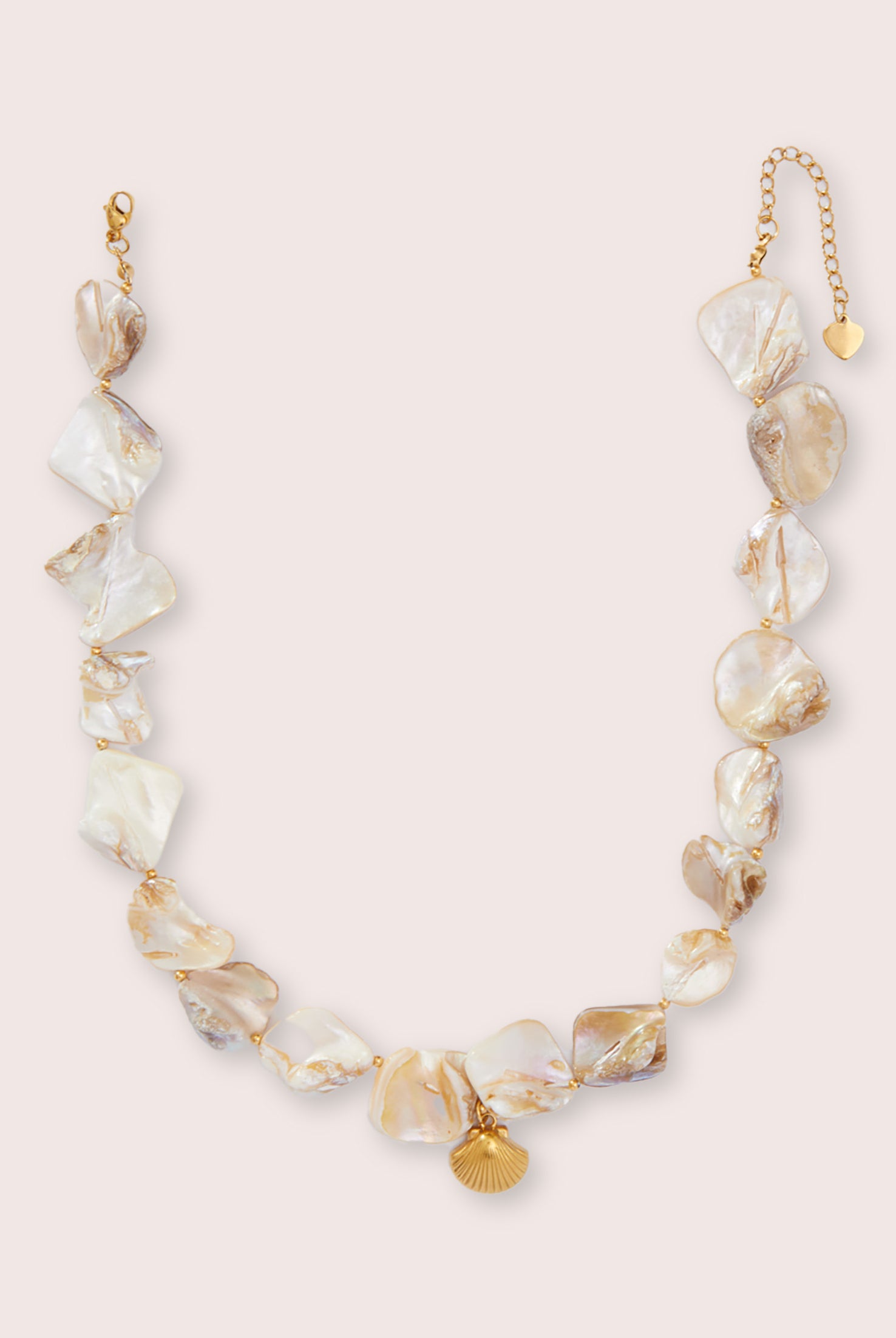 A necklace with small stones and gold shell piece against a white wall.