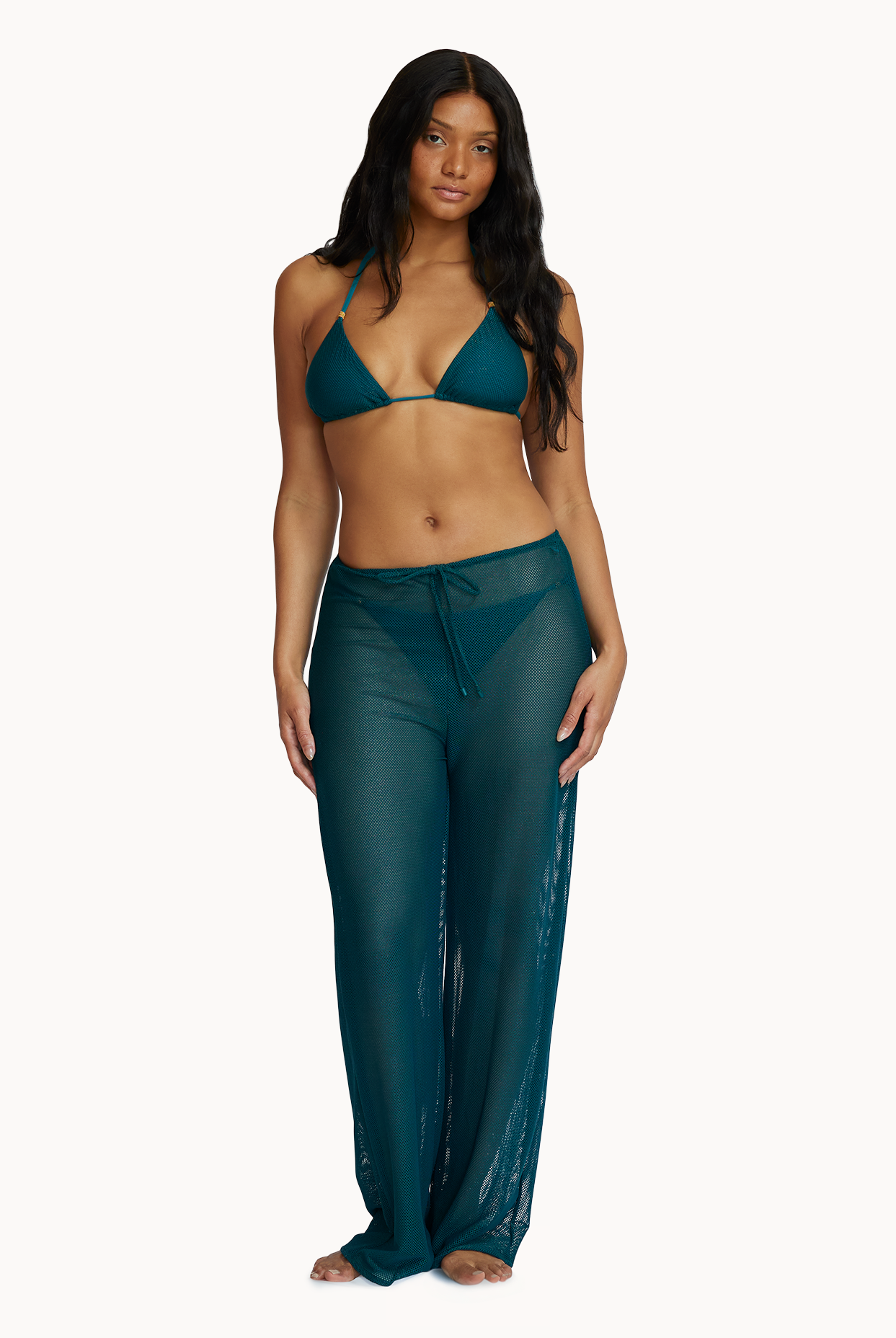 A woman wearing a green bikini top and matching pants against a white wall.