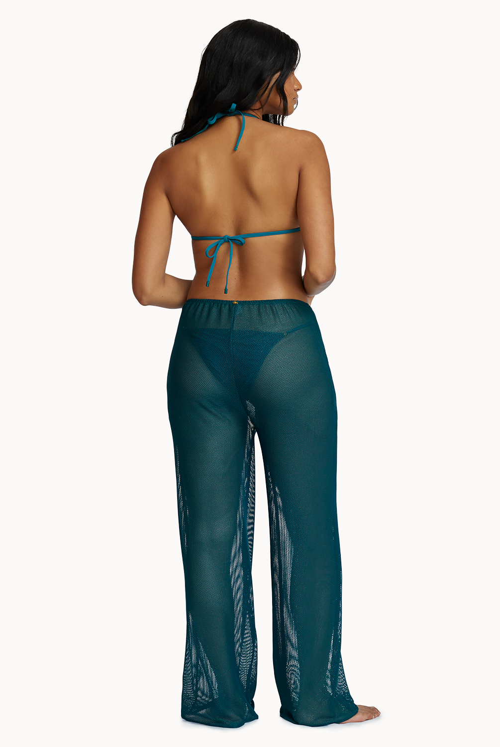 A woman wearing a green bikini top and matching pants facing towards a white wall.