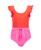 A pink and red color block kids one piece swimsuit against a white wall.