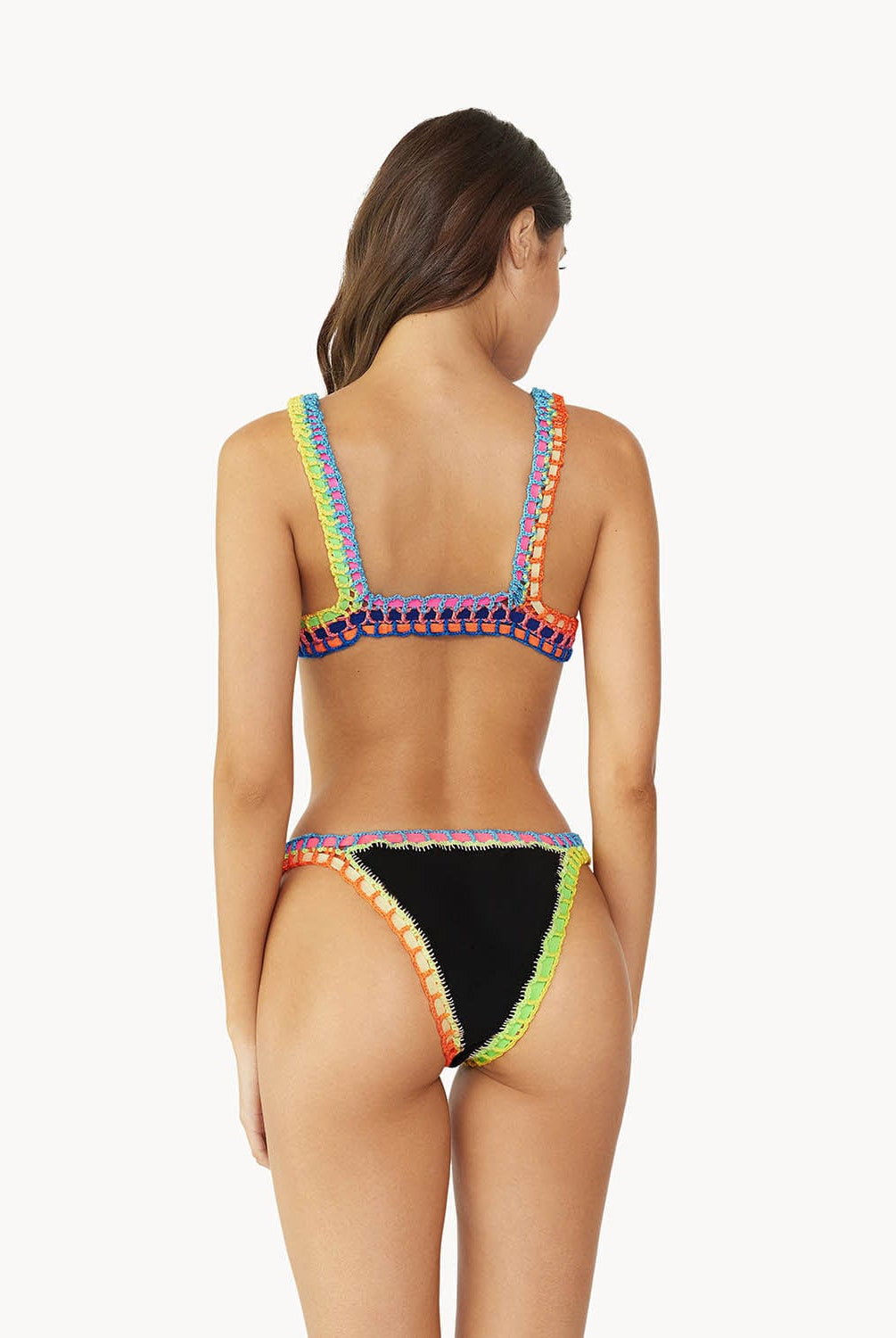 A brunette woman wearing a black bikini facing a white wall.