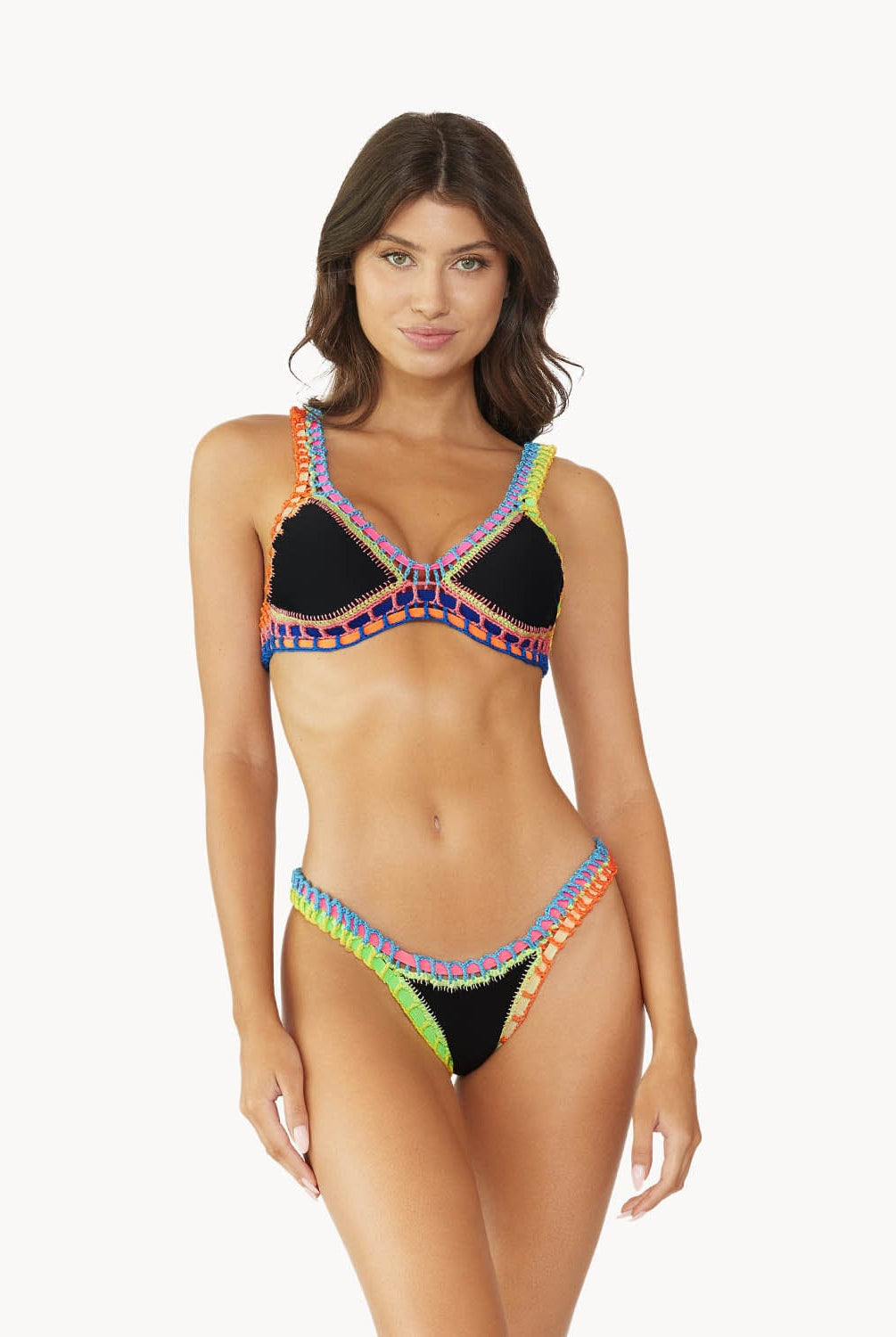 A brunette woman wearing a black bikini standing against a white wall.