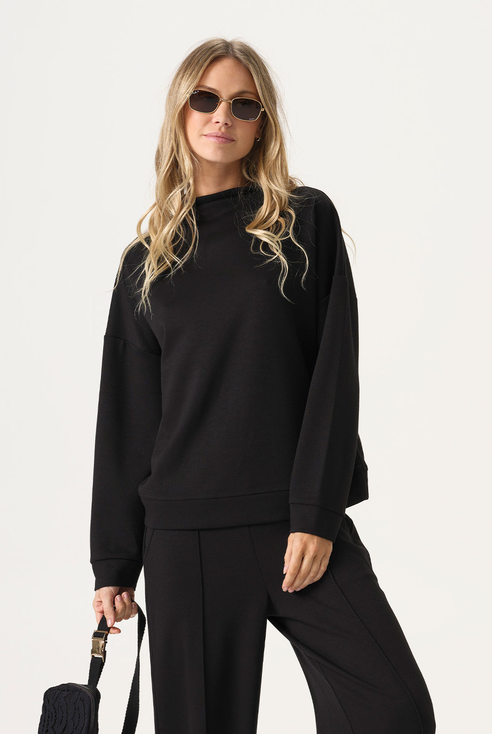 Woman wearing a black outfit with sunglasses on a white background