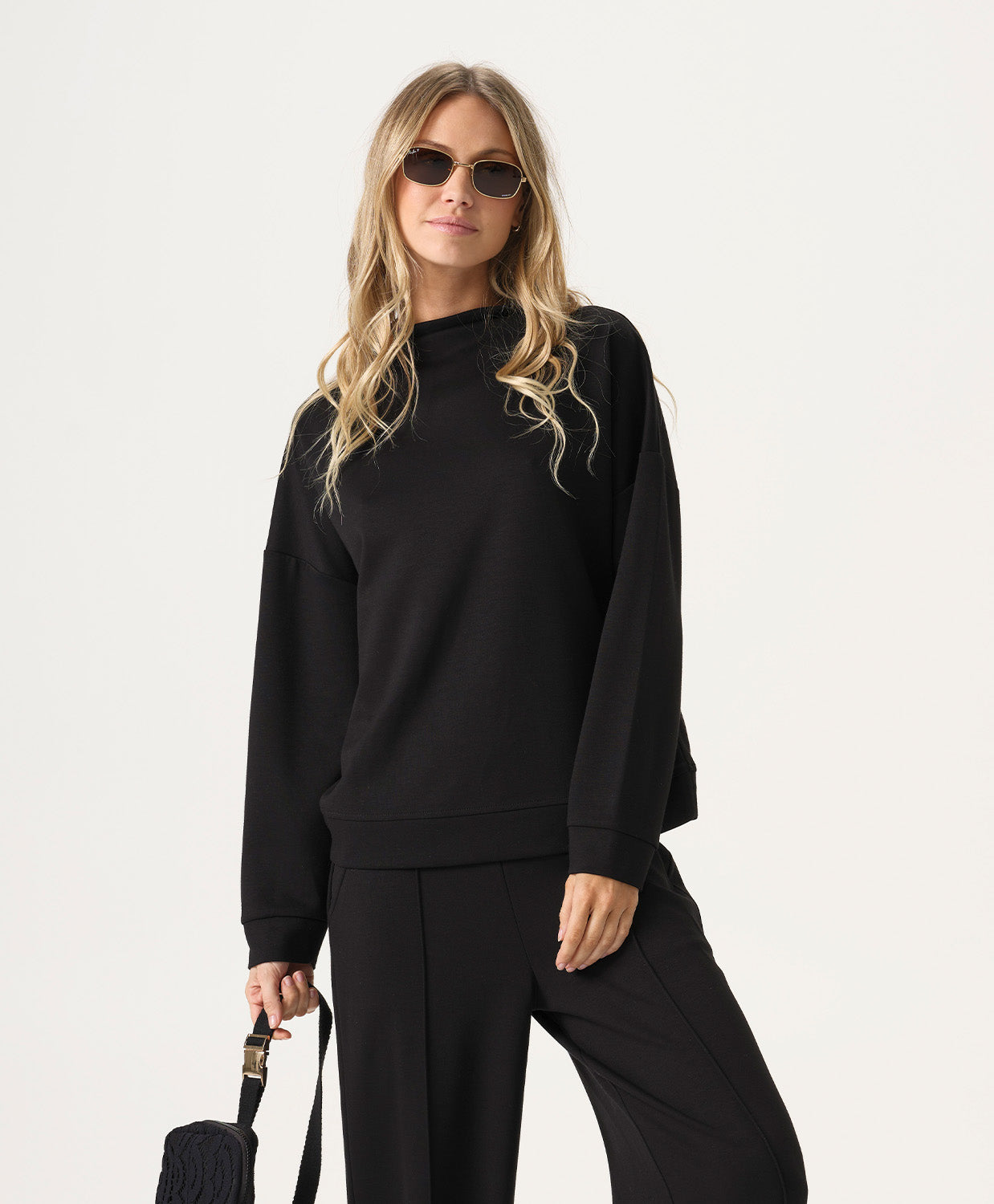 Woman wearing a black outfit with sunglasses on a white background