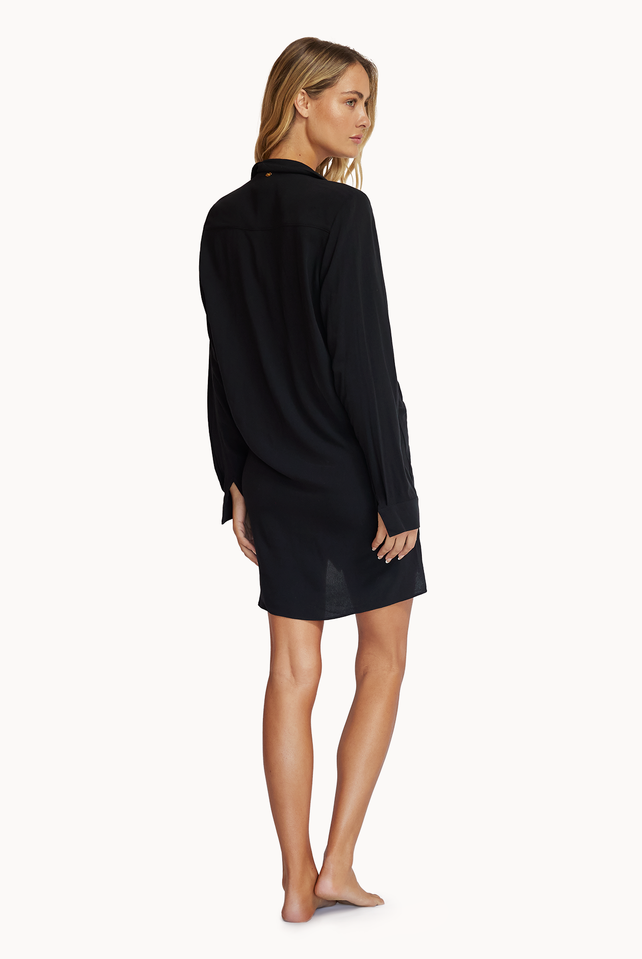 A woman wearing a black long sleeve cover up facing towards a white wall.