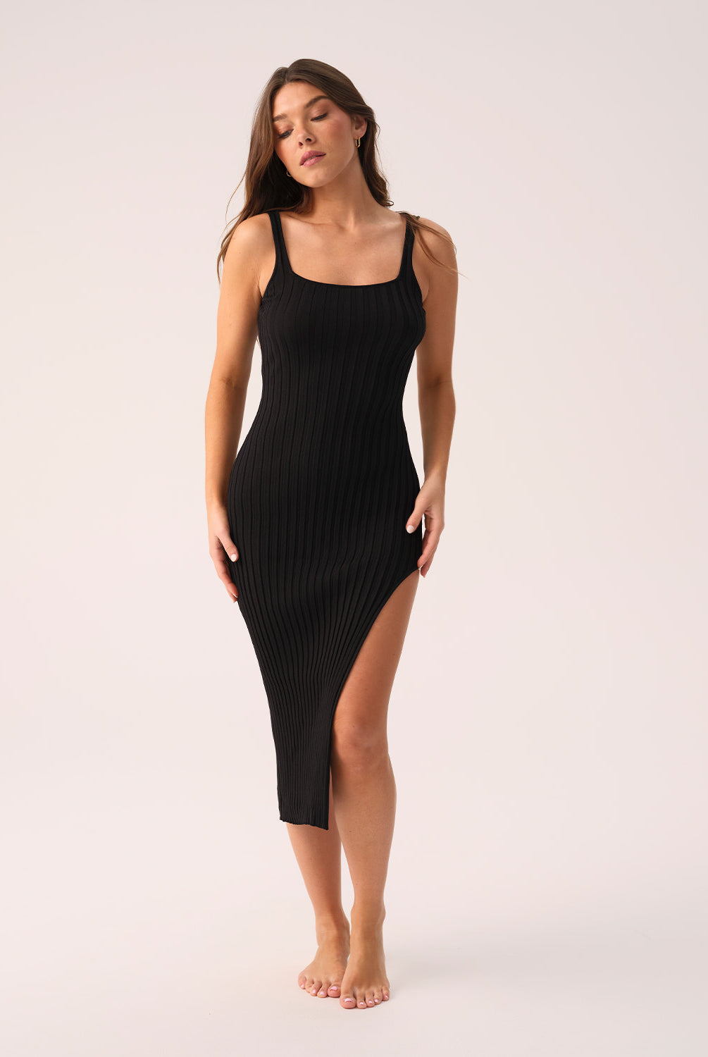 Woman wearing a black ribbed dress with a slit on a white background