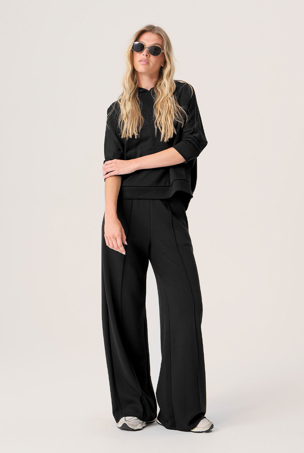 Woman wearing a black outfit with sunglasses on a plain background