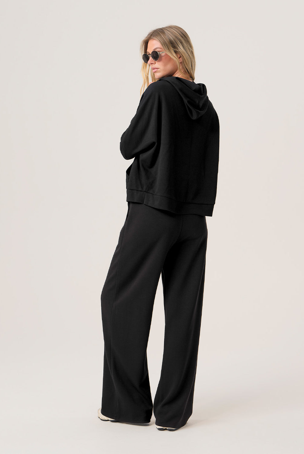 Woman wearing a black hoodie and black pants on a light gray background