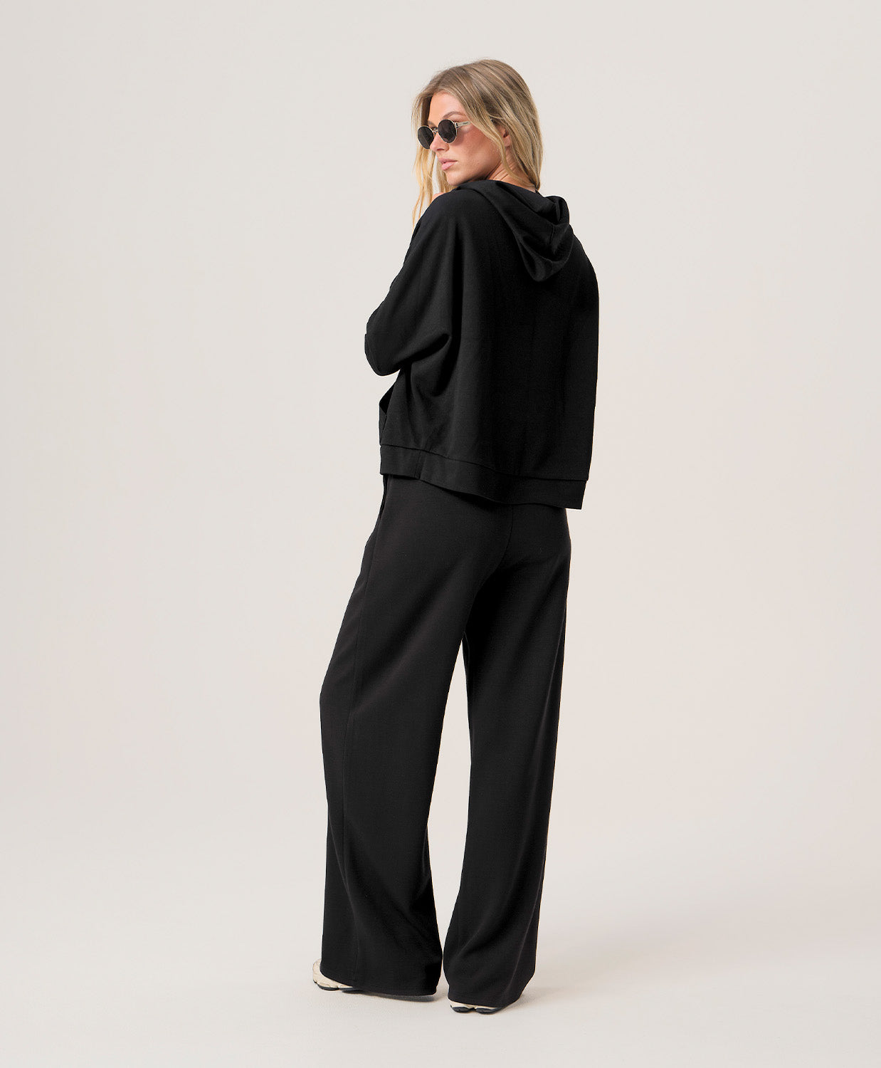 Woman wearing a black hoodie and black pants on a light gray background