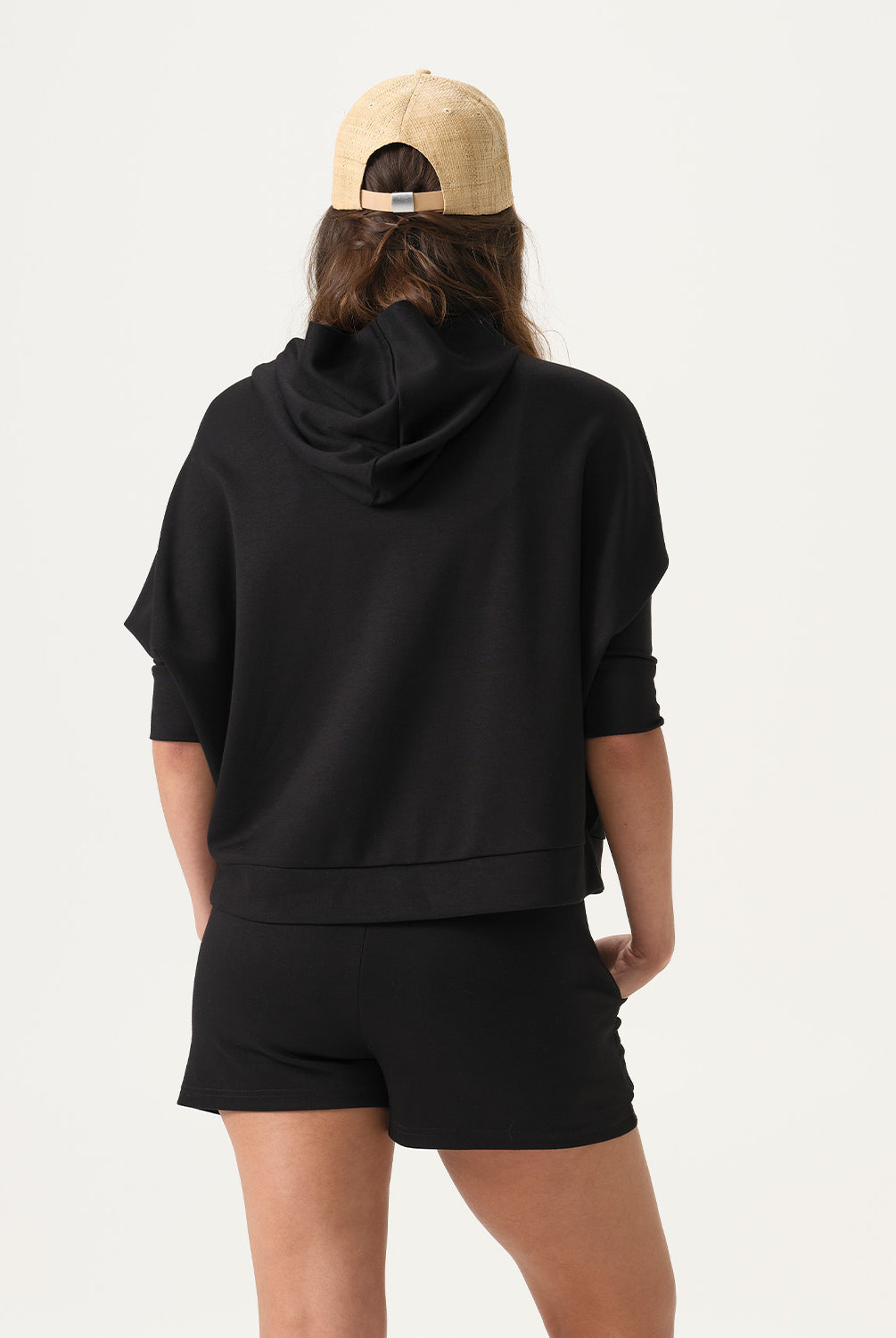 Woman wearing a black hoodie and shorts with a beige cap on a white background
