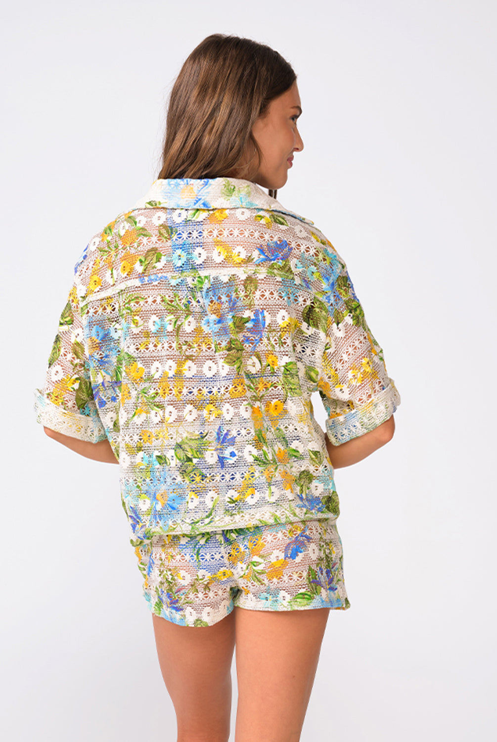 A woman wearing a matching floral shirt and shorts facing towards a white wall.