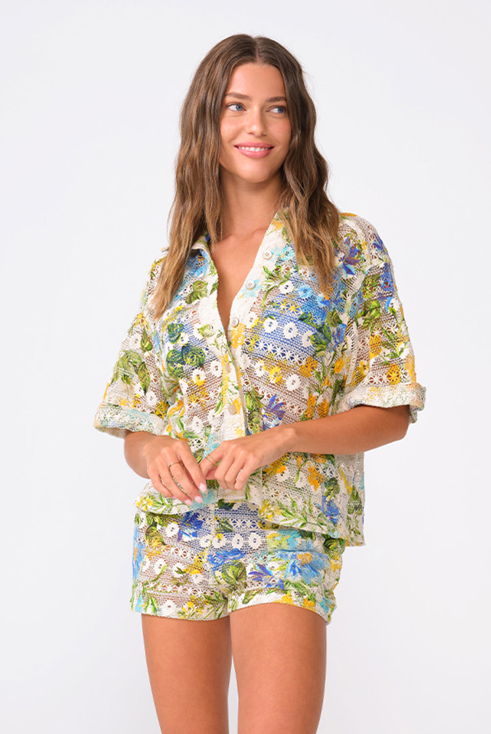 A woman wearing a matching floral shirt and shorts standing against a white wall.