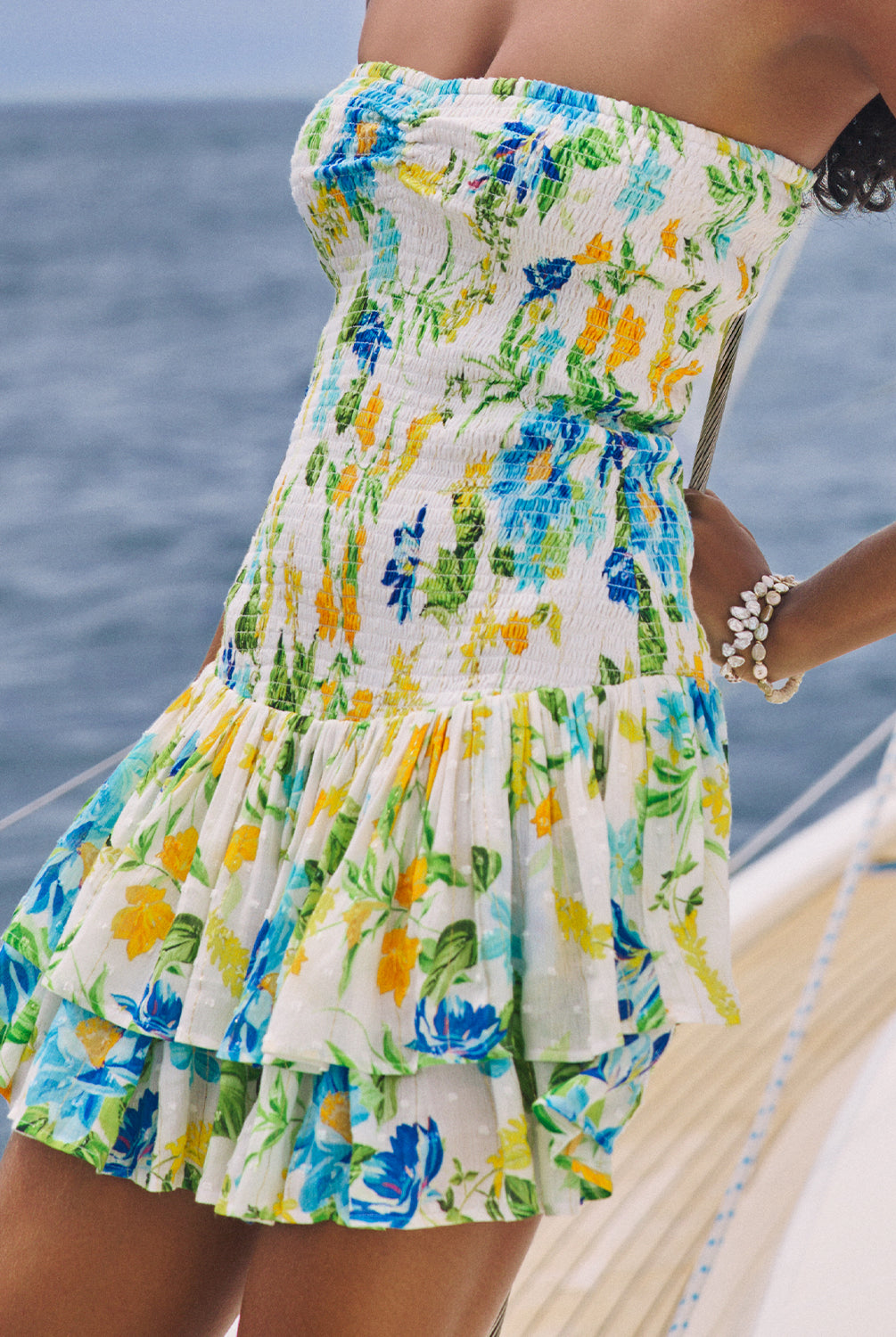 A woman wearing a short strapless floral dress standing on a boat on the ocean.