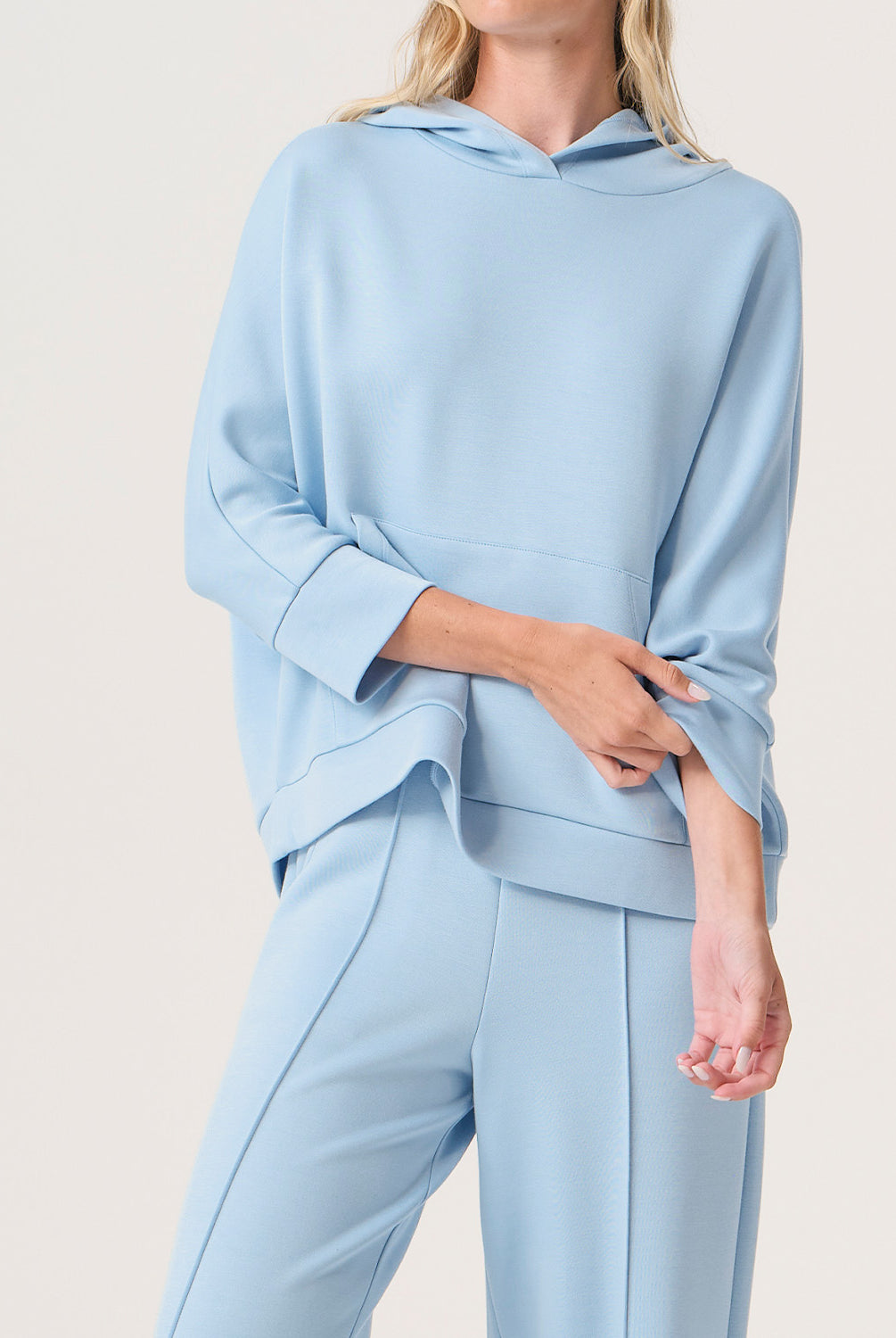 Woman wearing a light blue hoodie and pants set on a plain background