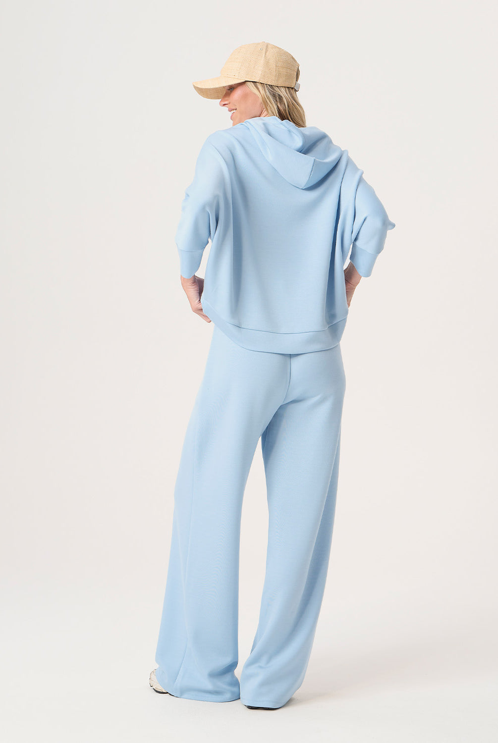 Woman wearing a light blue hoodie and pants with a beige cap on a white background