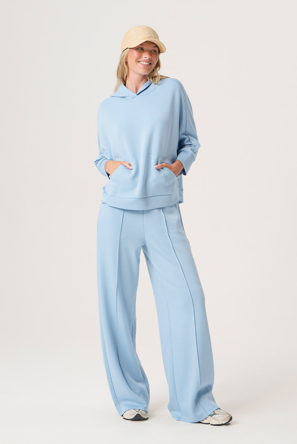 Woman wearing a light blue outfit with a beige cap on a white background