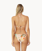 A blonde woman wearing a bikini wtih a tropical print facing towards a white wall.