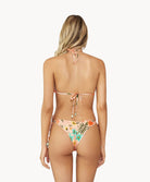 A blonde woman wearing a bikini wtih a tropical print facing towards a white wall.