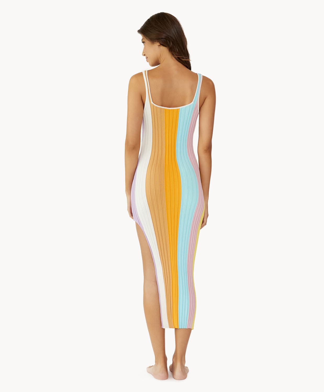 A brunette woman wearing a multi colored stripe dress facing towards a white wall.