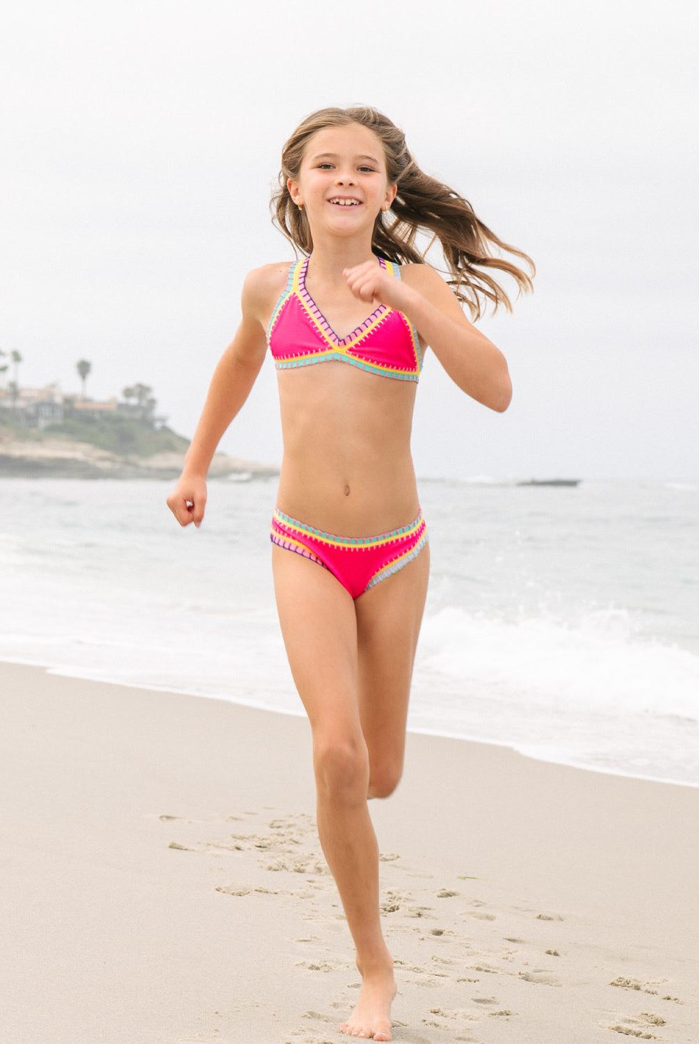 Young girl in a pink bikini running on a beach with ocean in the background
