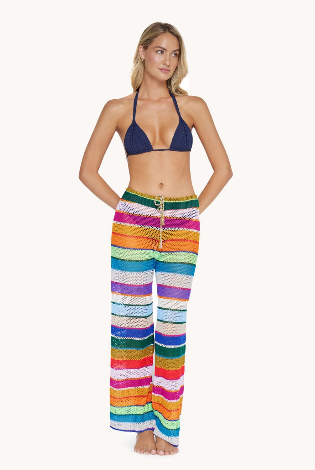 A blonde woman wearing a navy bikini top and color block pants standing in front of a white wall.